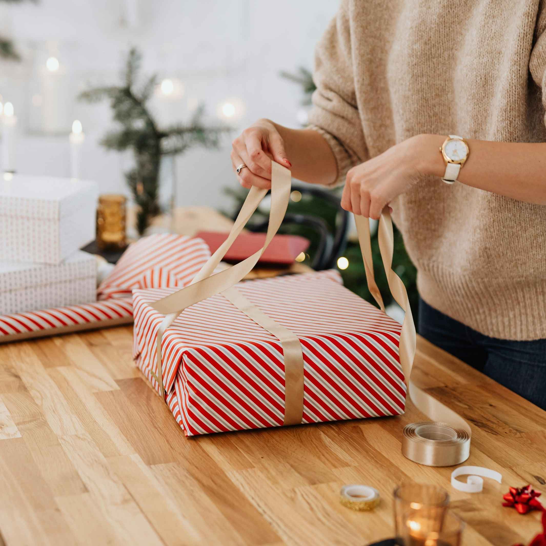 Woman wrapping a gift for a christmas party for collection of christmas party invitation templates on Canva by Simple Desert Designs.