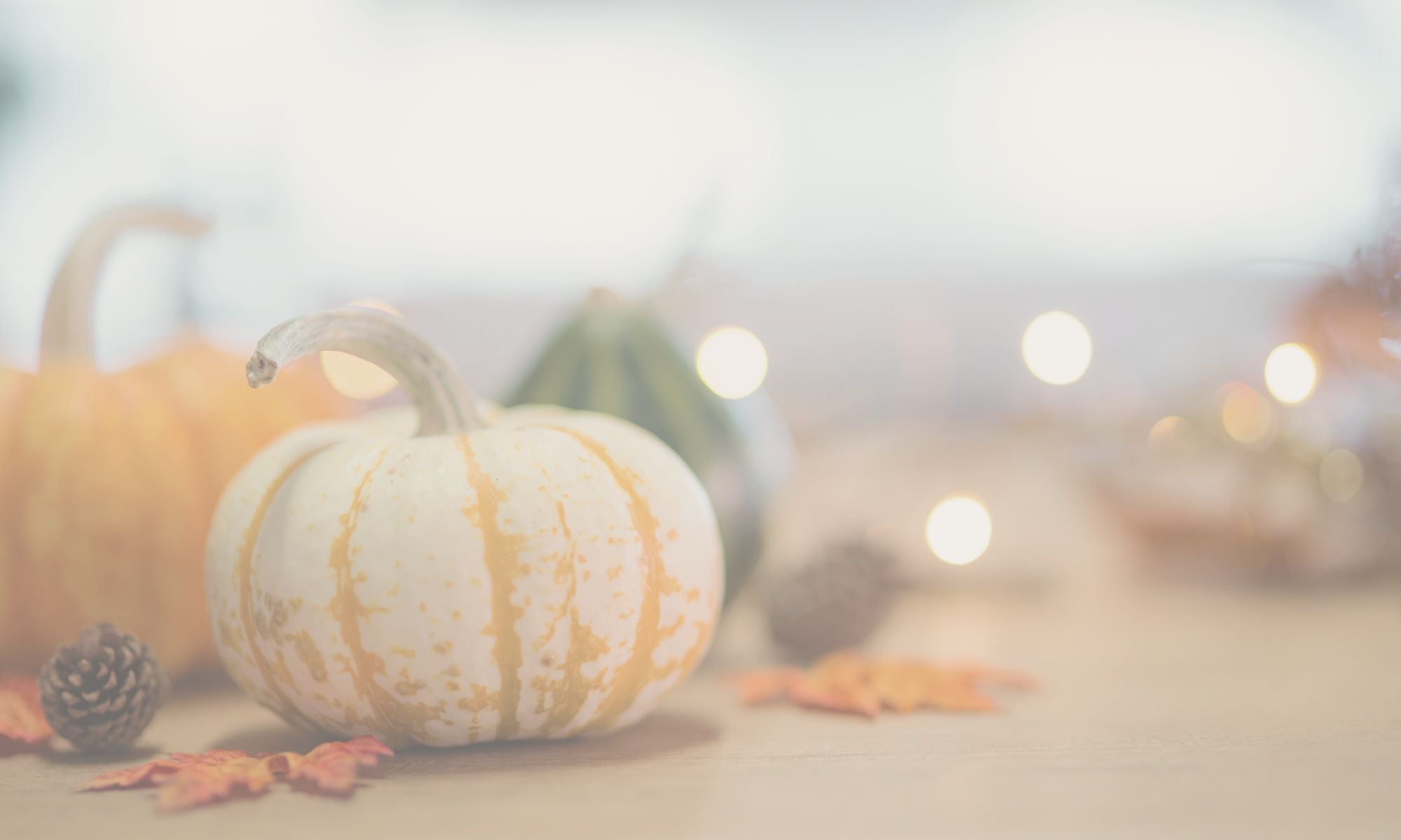 light wood table with pumpkins, lights and fall leaves