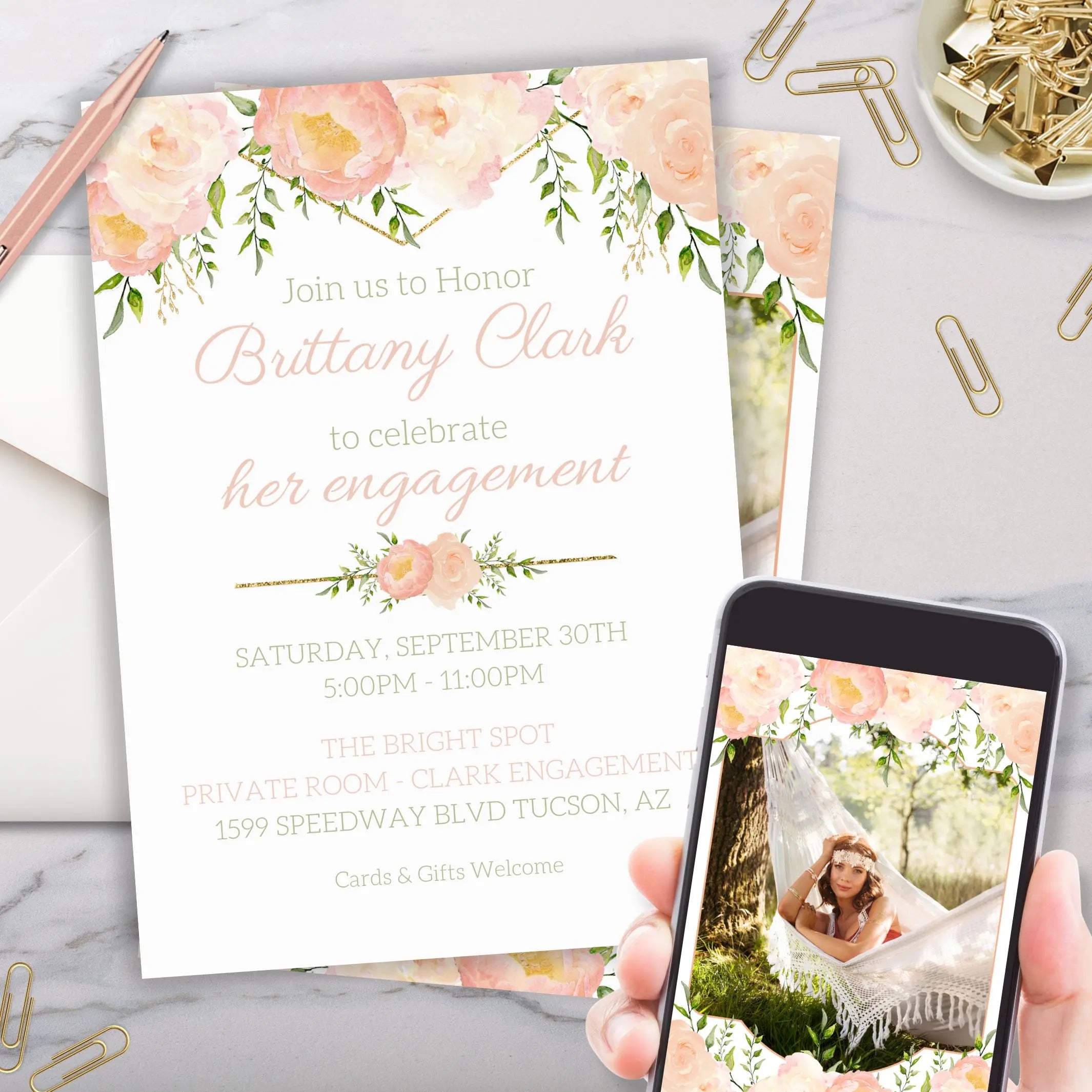 Elegant engagement party invitation card customized with photo with elegant peach and greenery floral design with gold accents held by a person using a phone.