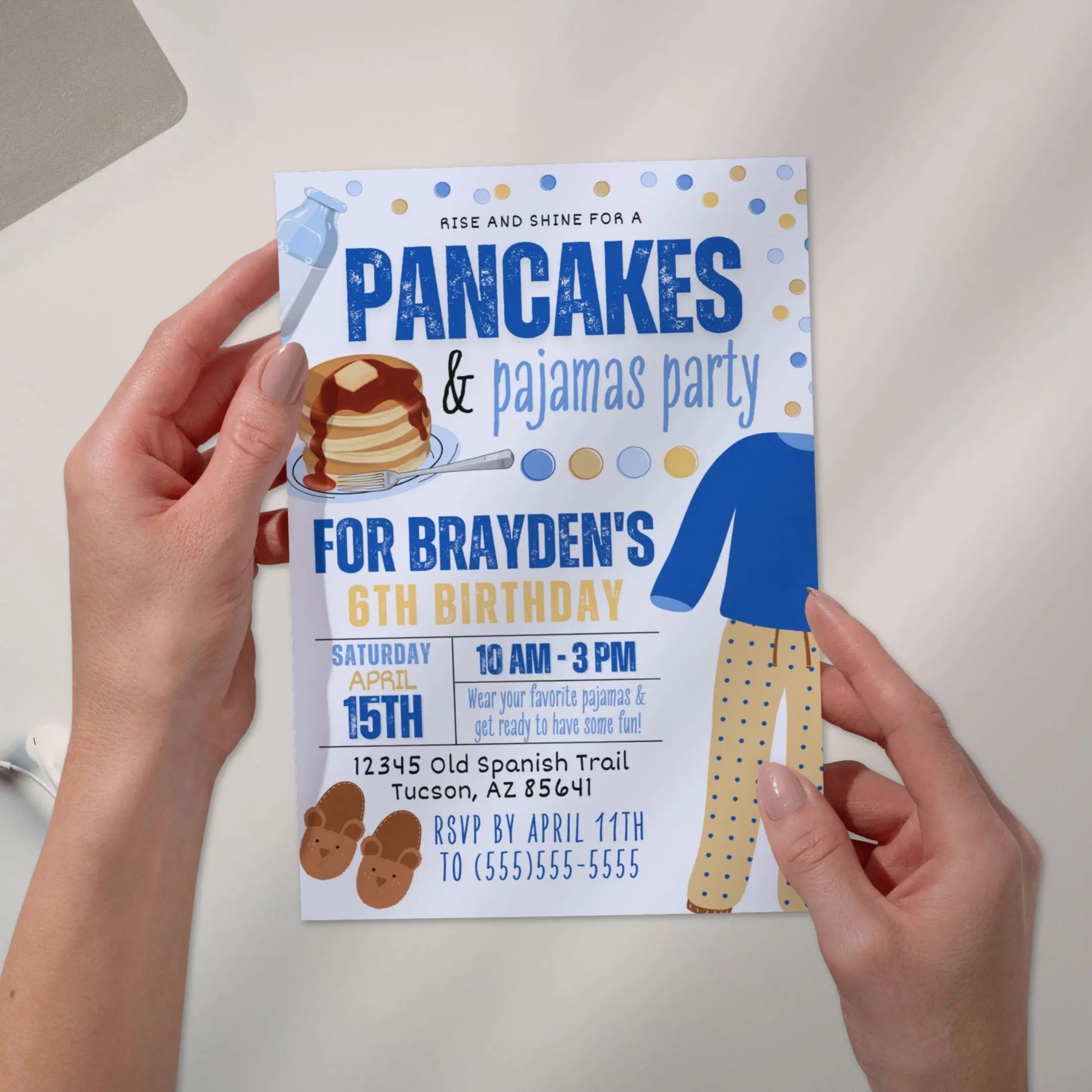 Hand holding a birthday party invitation with pancakes and pajamas theme personalized with boys name, age and party details.