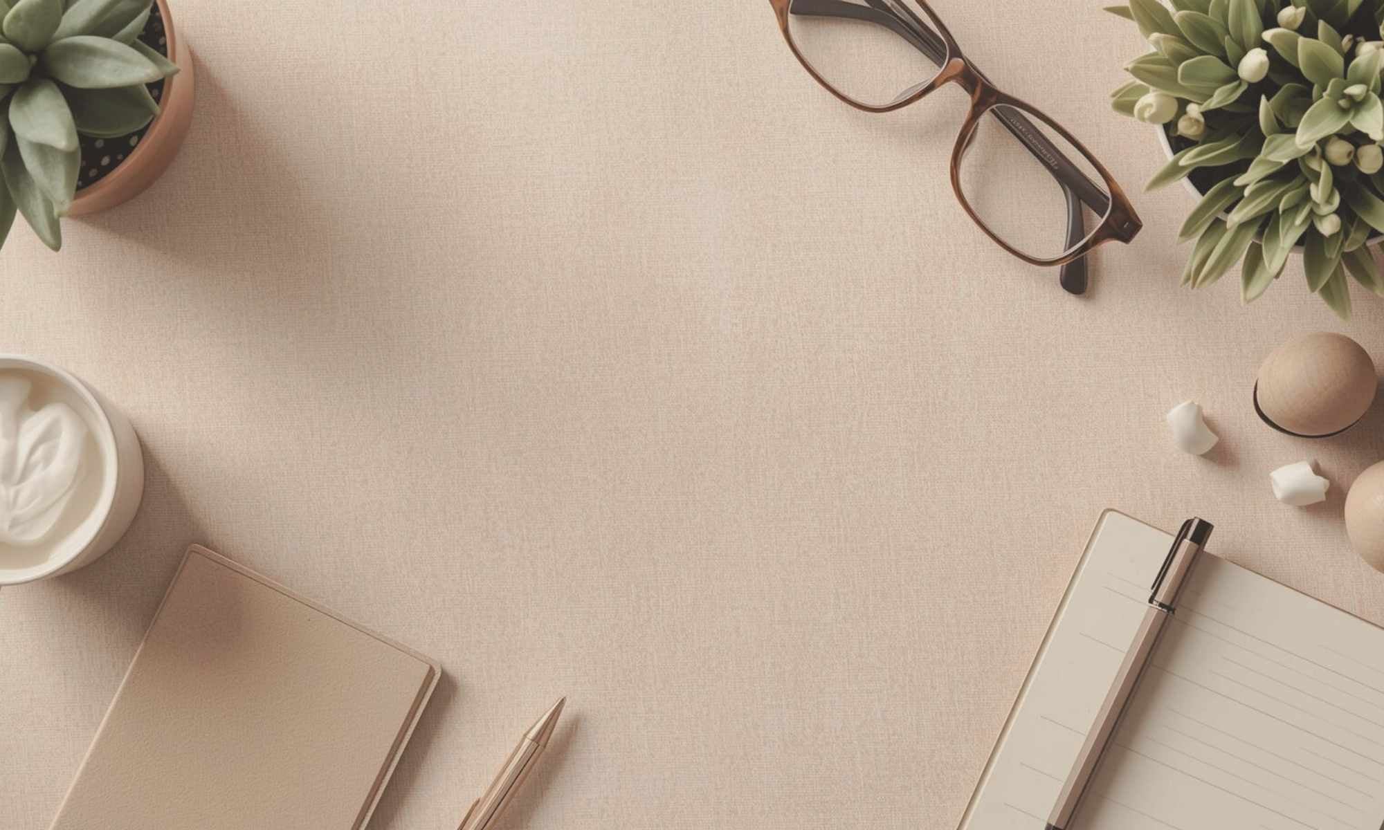neutral desk surface with notebook, pen, glasses, greenery plants and soft decor