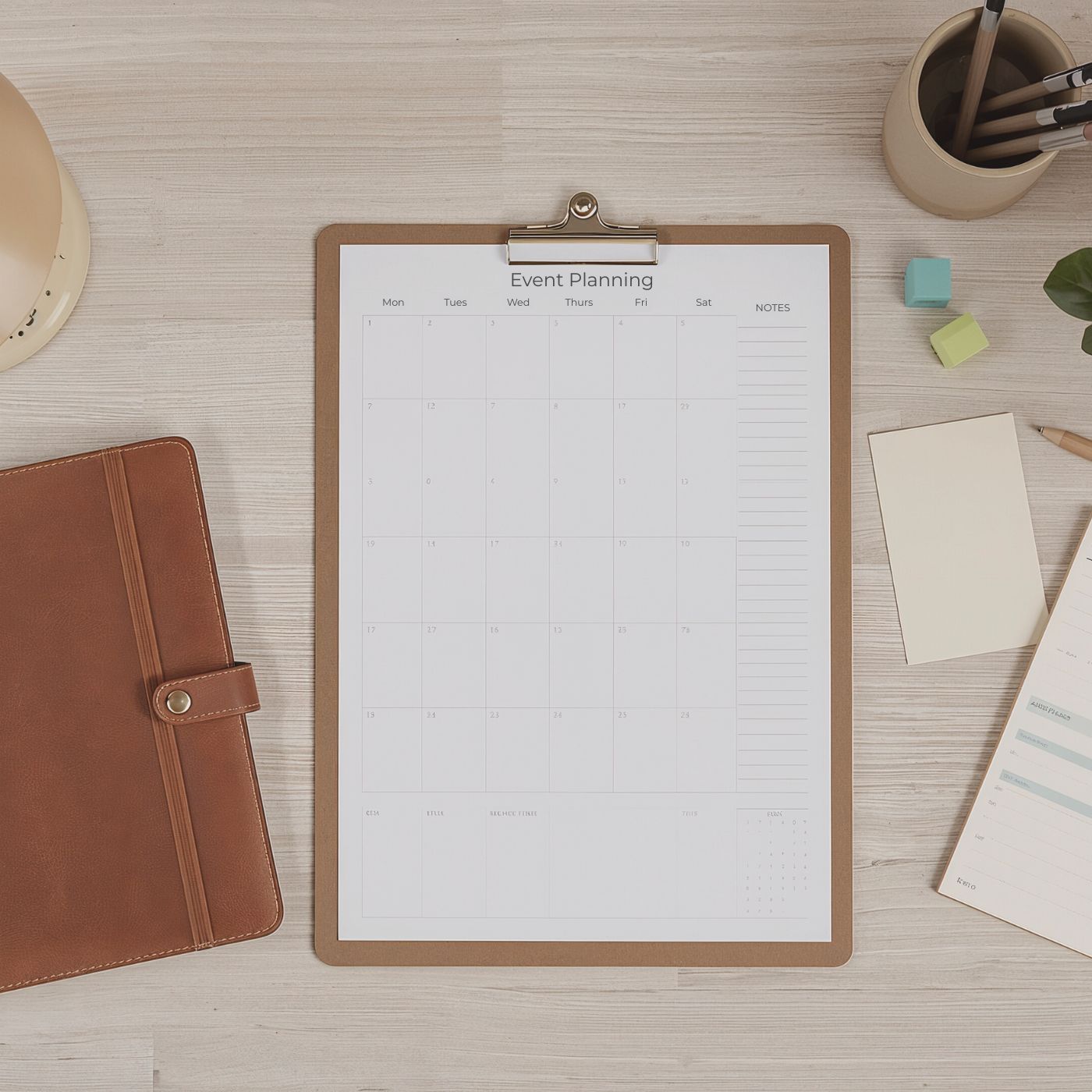 event planner on light wood desk surface with sticky notes and notebooks with pencils and pens