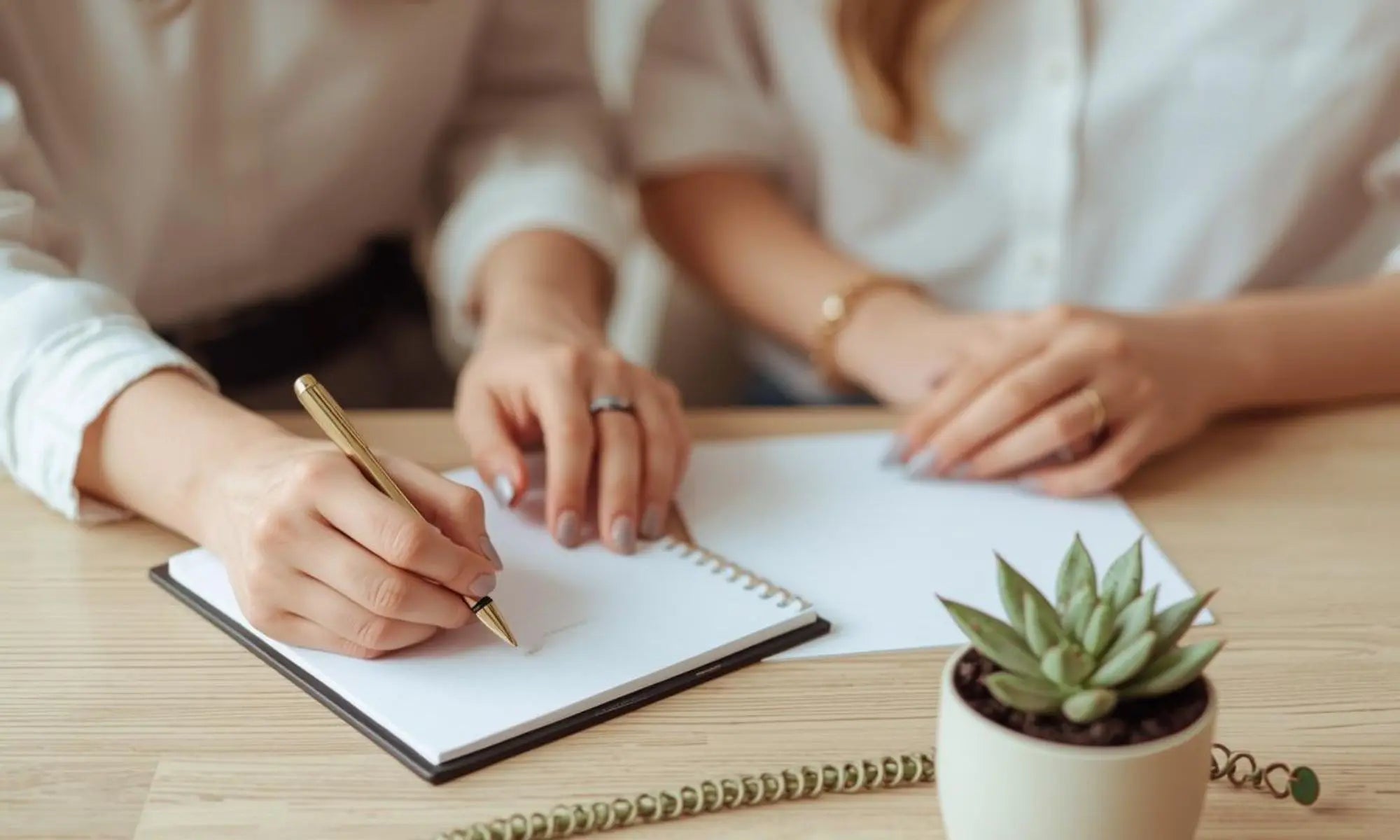 A close-up of two people collaborating with a pen and sketchbook on a minimalist wood desk, representing the Giving Back Through Creativity program for nonprofit custom design.