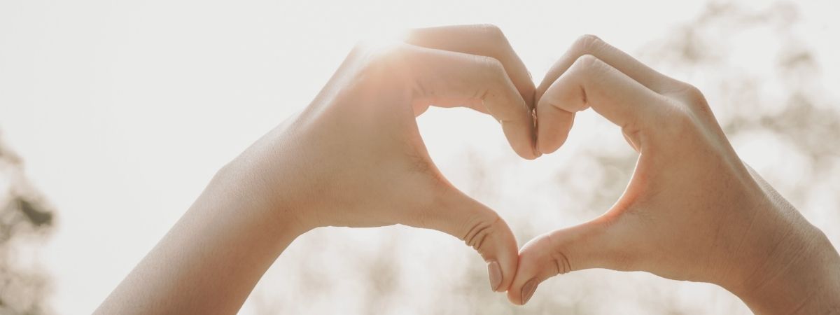 Two hands making a heart shape against a blurred natural background to signify community outreach and giving back.