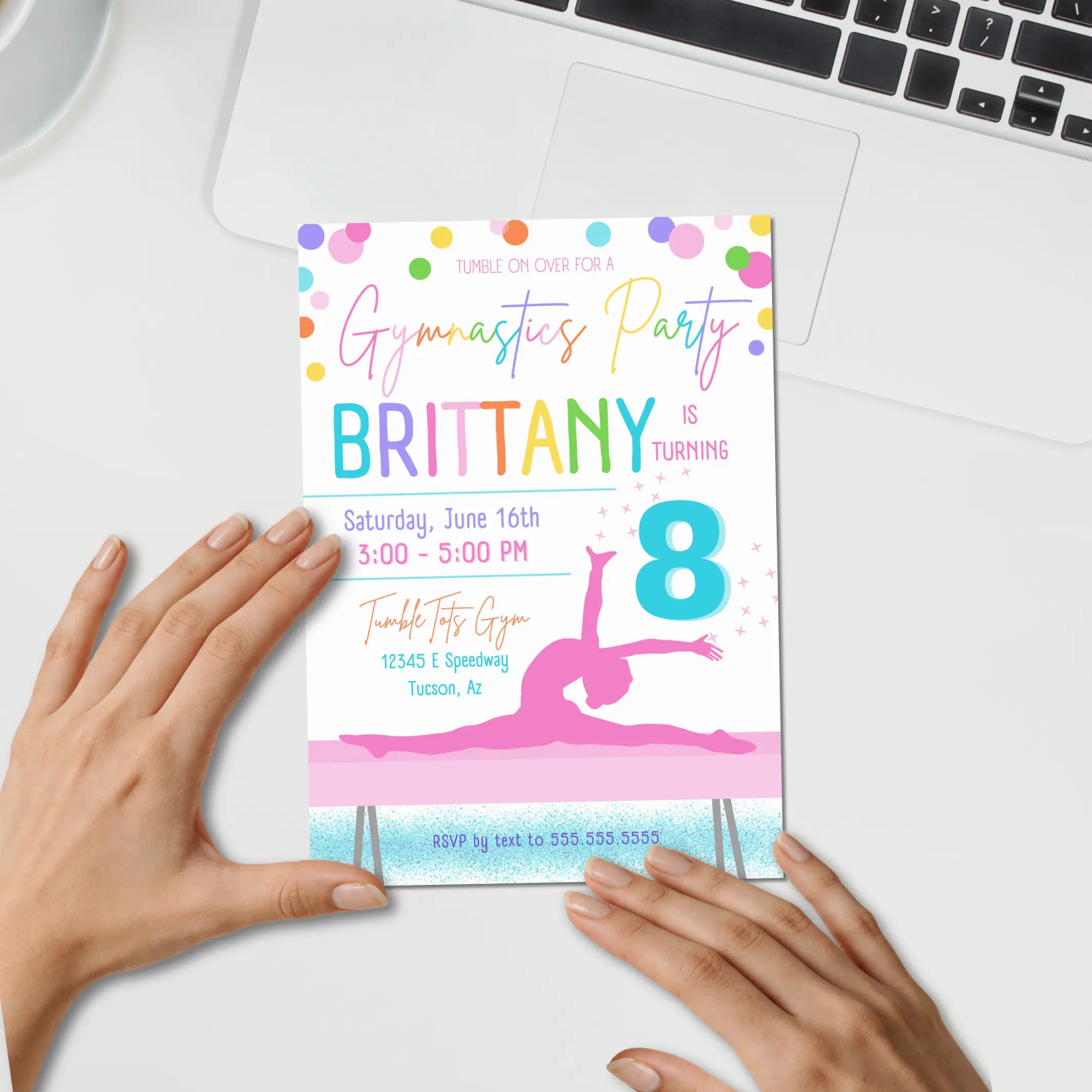 Image of an editable gymnastics party invitation held by hands on a white surface with a laptop.