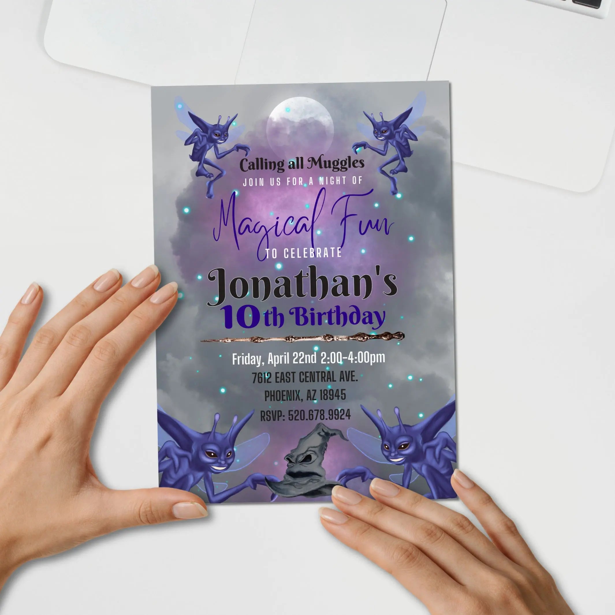 Hand holding a customized editable invite template for a birthday invitation with magical pixie design elements, magic hat and wand on a white surface