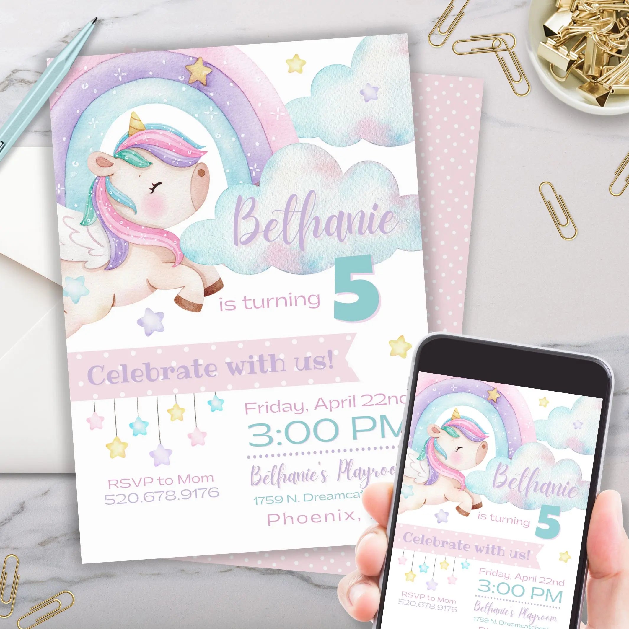 Pastel unicorn-themed birthday invitation card customized with age on it with a phone displaying the same design on a marble surface.