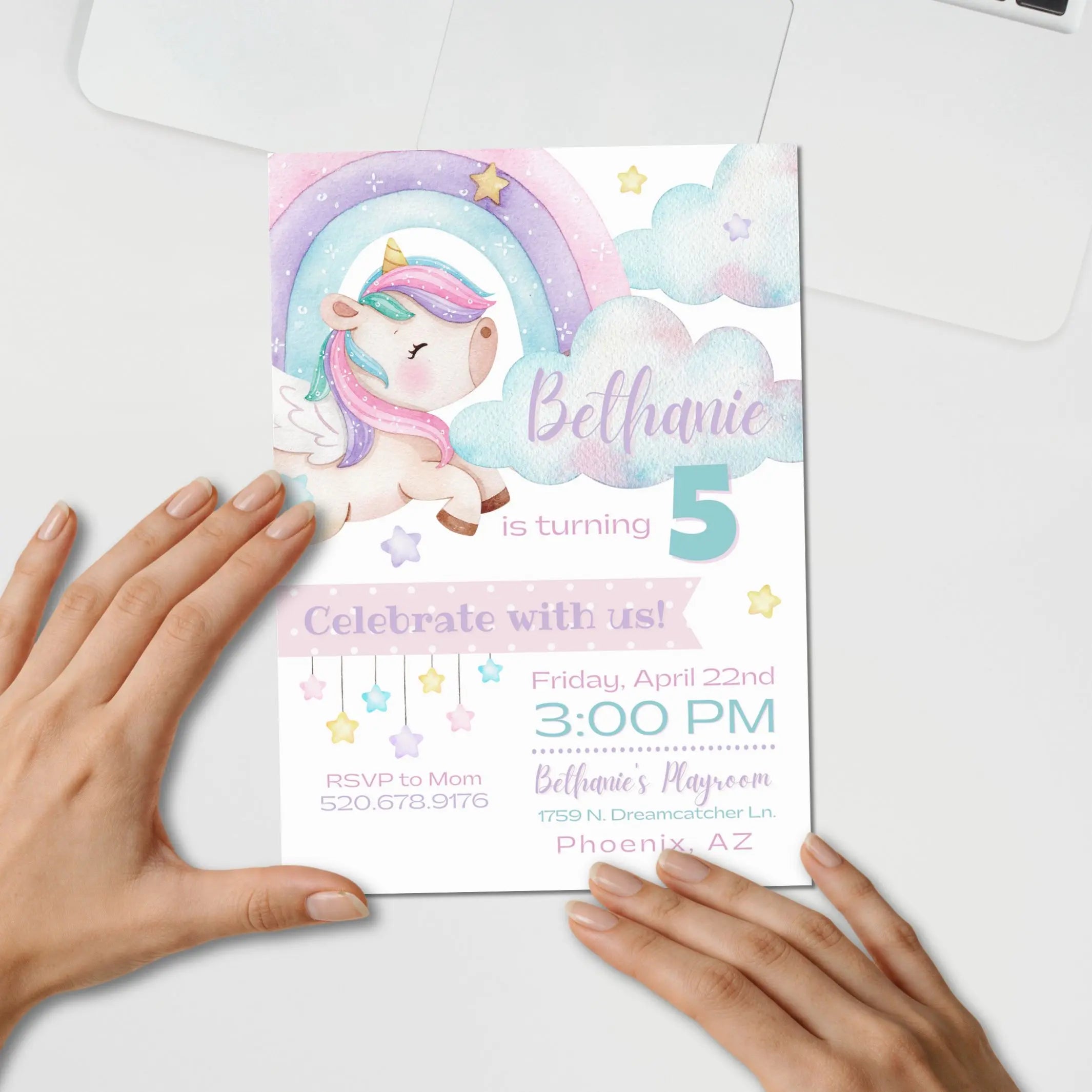 Pastel glitter unicorn birthday invitation card customized with unicorn, clouds and stars design held by hands on a white surface